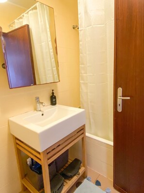 Ein Badezimmer mit Waschbecken, Spiegel, Duschvorhang und Holztür.