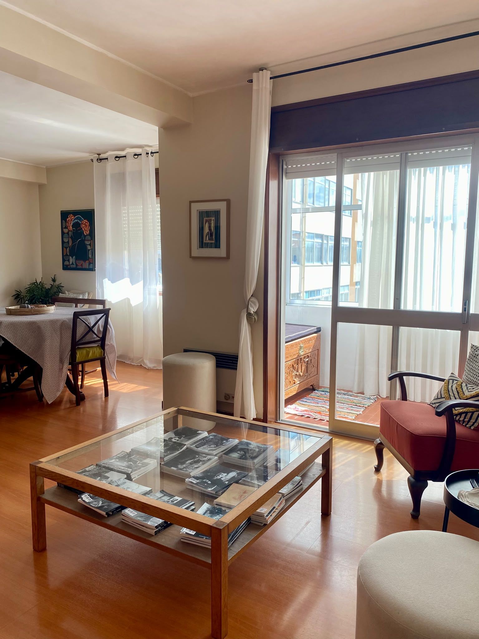 Ein Wohnzimmer mit Glastisch, ein Essbereich mit Tisch und Stühlen sowie ein großes Fenster mit Vorhängen.