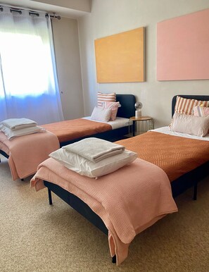 A hotel room with two beds, each with a patterned bedspread and pillows, a small round table with a lamp, and a large window with curtains. - Elegant and spacious apartment by the sea! (Póvoa de Varzim)
