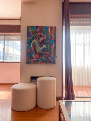 Relax in a stylish space with a vibrant abstract painting, comfortable seating, and a large window offering a view of the outside.
