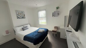 A bedroom with a bed, a television, a window, and a small shelf.