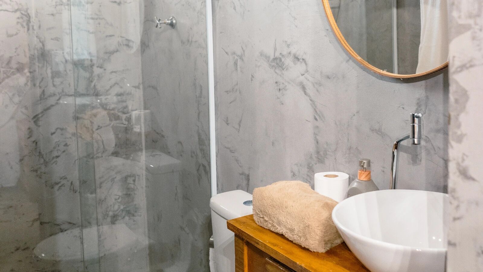 A bathroom with a marble shower, a toilet, a sink, and a mirror.