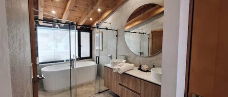 Un baño moderno con cabina de ducha de vidrio, bañera independiente y tocador con un espejo grande.