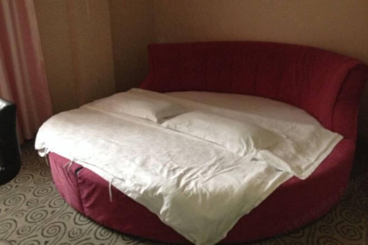 Ein rotes Schlafsofa mit weißem Bezug, ein gemusterter Teppich und eine schlichte Wand.