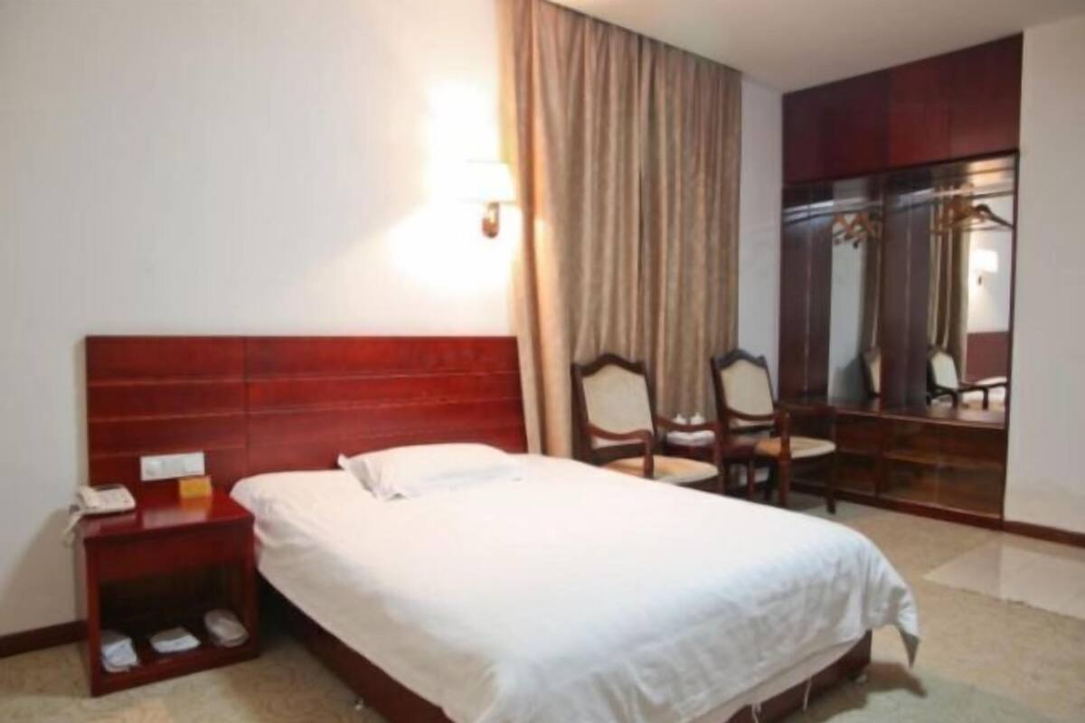 Ein Hotelzimmer mit Bett, Nachttisch, Stuhl, Spiegel und Kleiderschrank.