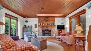 A cozy living room with a fireplace, checkered sofas, and a wooden ceiling.