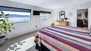 Ein Schlafzimmer mit großem Fenster, einem Bett, einem Schminktisch, einem Spiegel und einer kleinen Sitzecke.