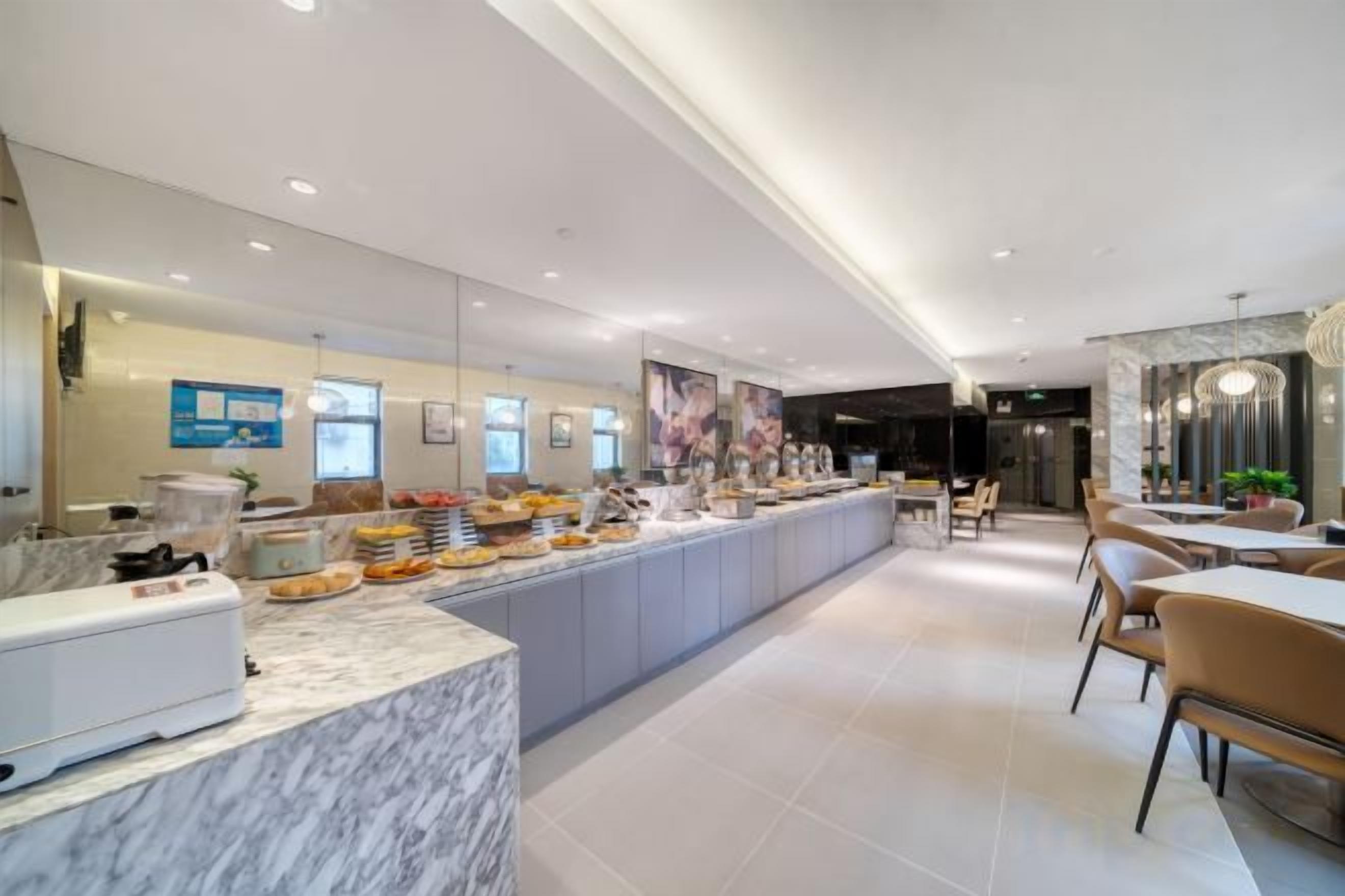 A modern hotel lobby with a marble reception desk, a buffet area, and a seating area with tables and chairs.