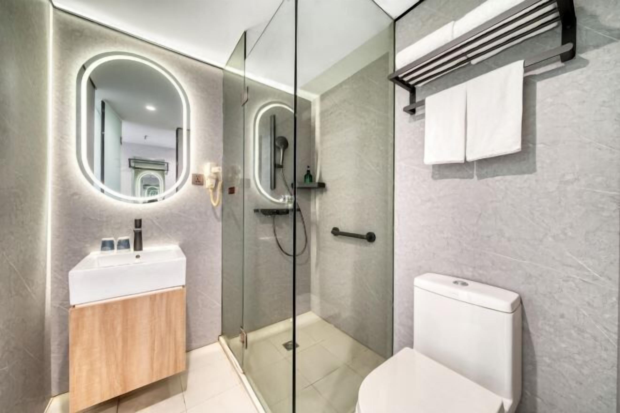 Un baño moderno con ducha envuelta en vidrio, un lavamanos blanco y un inodoro.