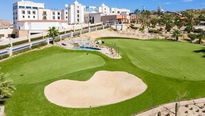 Ein Golfplatz mit einem großen Bunkersand, einer Wassergefahr und einem Gebäude mit mehreren Stockwerken und Kuppelarchitektur im Hintergrund.