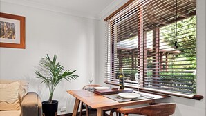 A dining area with a wooden table, chairs, a potted plant, and a window with blinds.