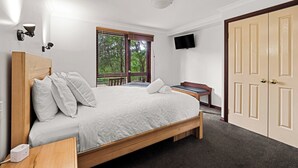 A bedroom with a bed, bedside table, lamp, window, and a TV mounted on the wall.