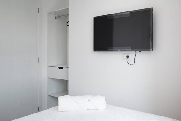 A hotel room with a bed, a white towel, a TV mounted on the wall, and a white wardrobe.