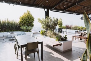 An outdoor patio area with a dining table and chairs, surrounded by various plants and a seating bench.