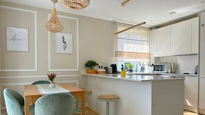 Een moderne keuken met een centraal eiland, barkrukken, een eettafel met stoelen, hanglampen en een raam met uitzicht.