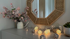 Een wastafel met spiegel, een vaas met roze bloemen en decoratieve verlichting.
