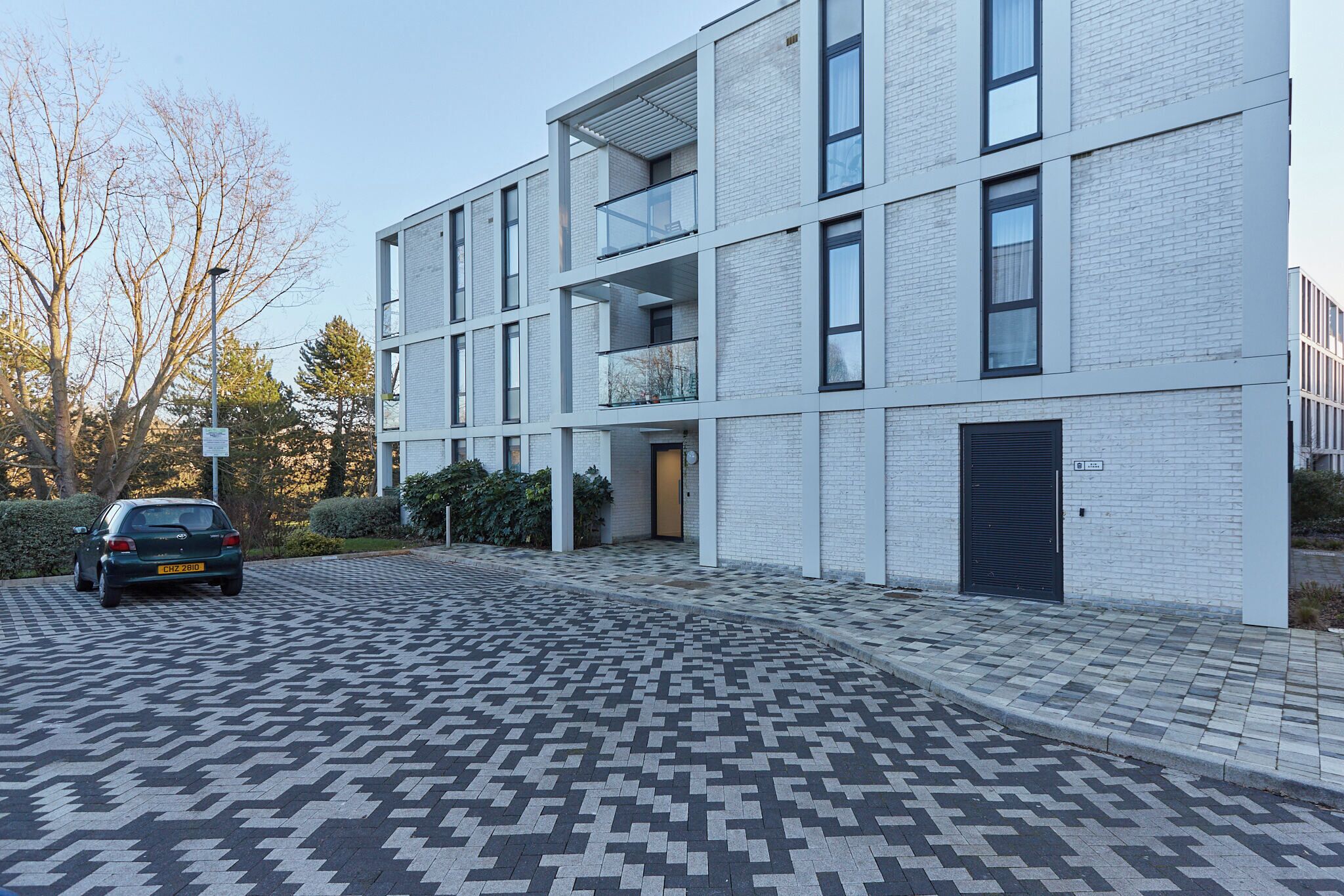 A modern building with a brick facade, multiple balconies, and a patterned driveway.