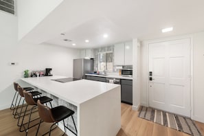 Una cocina moderna con una isla central, taburetes de bar, un refrigerador y un microondas.