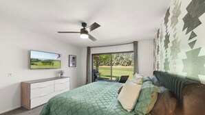 A bedroom with a bed, a ceiling fan, a TV, a dresser, and a view of a golf course through a sliding glass door. - Brand new fully remodeled house in Palm Desert w/ golf course views-Pet Friendly (Palm Desert)
