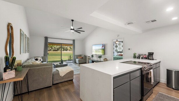 A modern kitchen with a central island, a dining area with a sofa, and a large window offering a view of the outdoors. - Brand new fully remodeled house in Palm Desert w/ golf course views-Pet Friendly (Palm Desert)