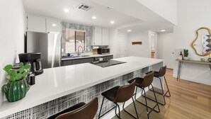 A modern kitchen with a large island, bar stools, and a coffee machine. - Brand new fully remodeled house in Palm Desert w/ golf course views-Pet Friendly (Palm Desert)