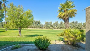 A well-maintained golf course with a clear sky, palm trees, and a building in the background. - Brand new fully remodeled house in Palm Desert w/ golf course views-Pet Friendly (Palm Desert)