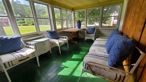 Een zonnedak met een houten tafel, twee stoelen, een bank en uitzicht op een groen landschap.