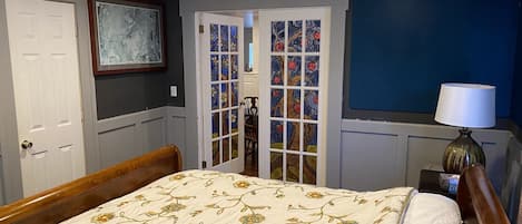 A bedroom with a bed, a door, a window, and a lamp.
