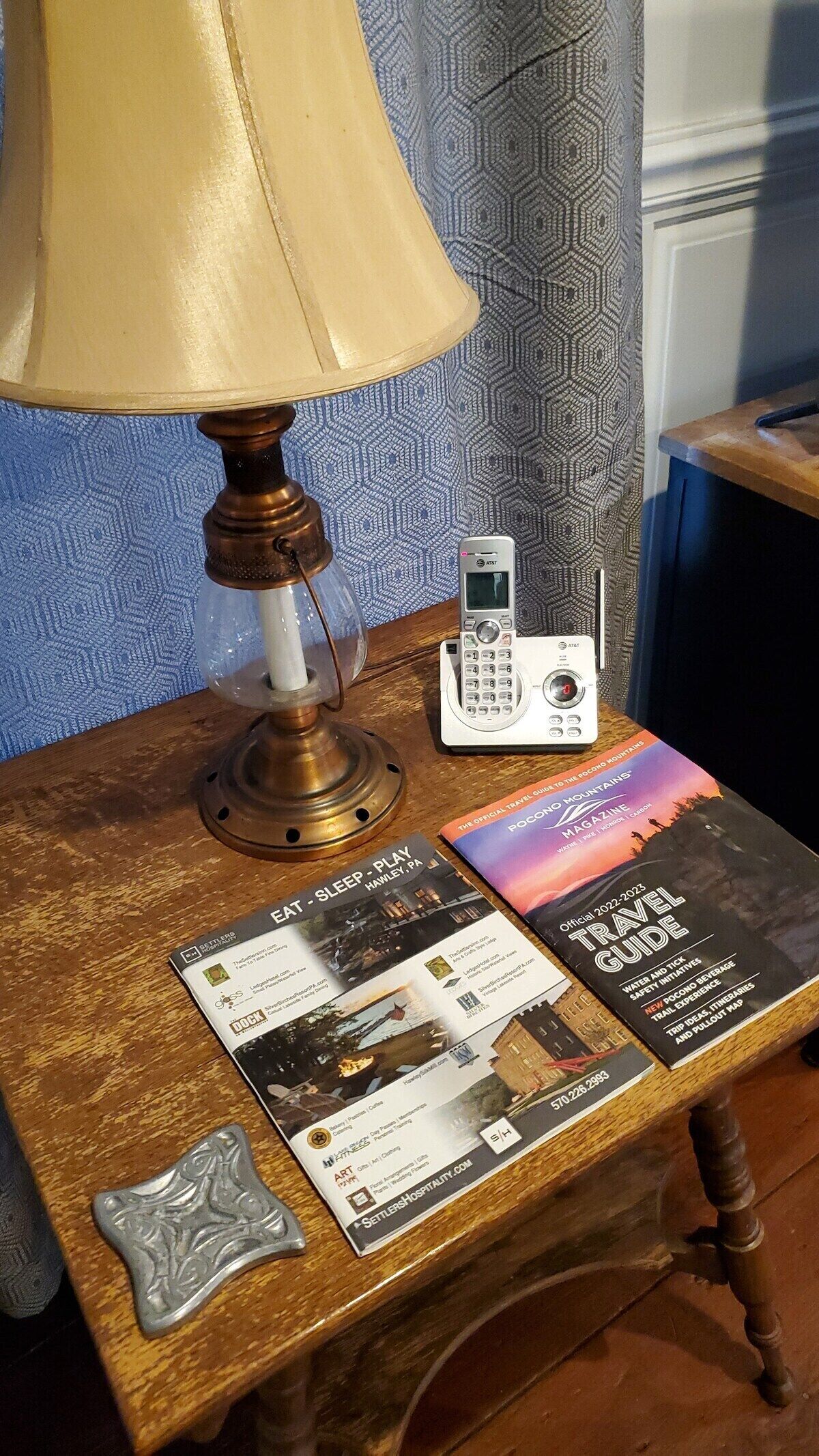 A wooden table with a lamp, a landline phone, and travel guides.