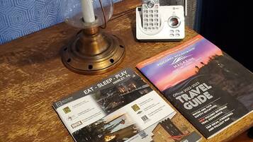 A wooden table with a lamp, a landline phone, and travel guides.
