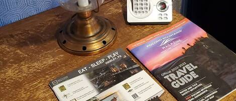 A wooden table with a lamp, a landline phone, and travel guides.