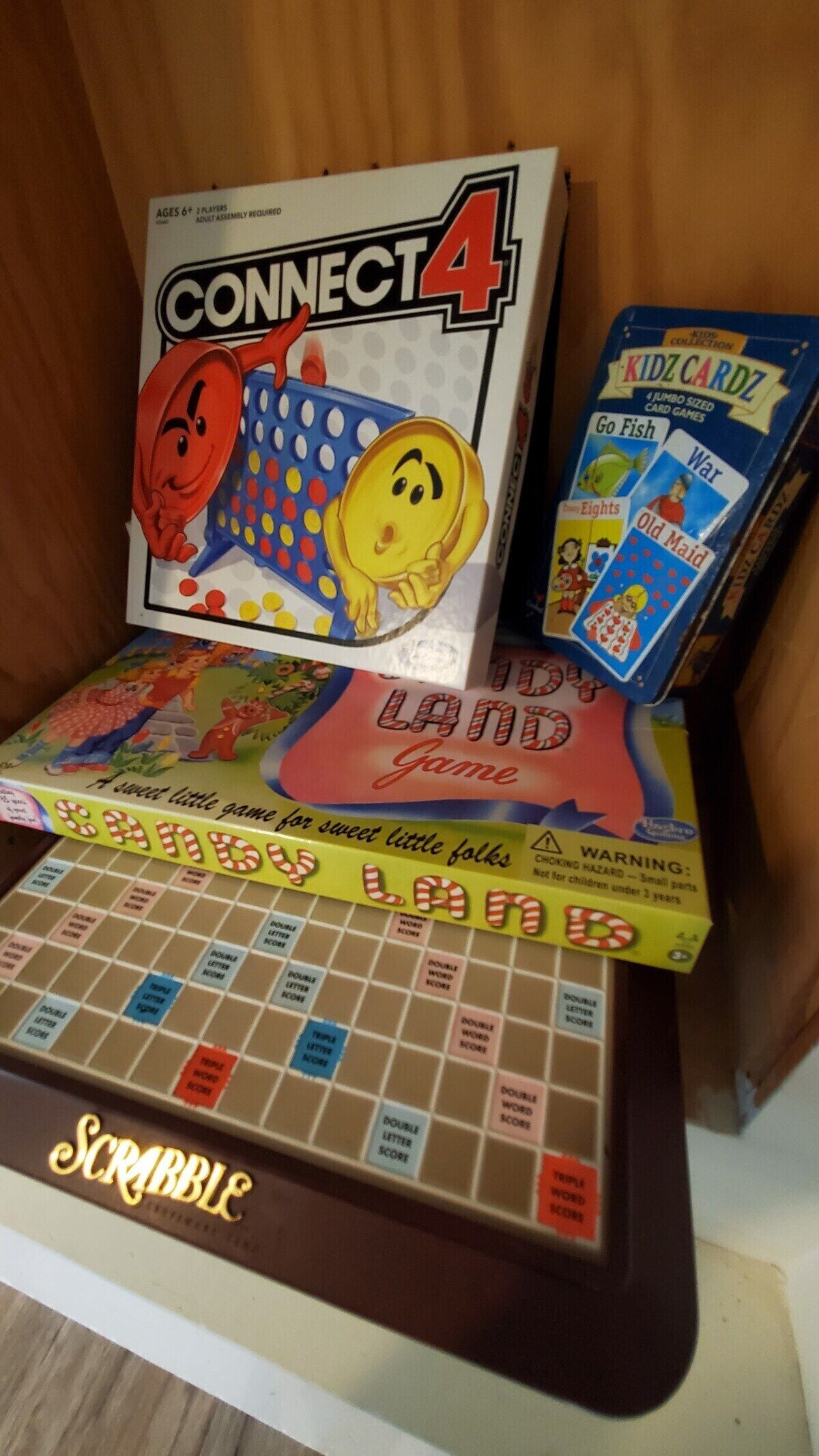A Connect 4 game box, a Scrabble board, and a Kidz Cardz pack.