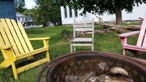 Een rustieke buitenruimte met een metalen vuurkuil, een Adirondack-stoel in geel en een Adirondack-stoel in roze.