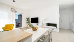 A modern, minimalist living room with a white color scheme, a dining area with a wooden table, and a fireplace. - Seaview apartment Lana (Seget Donji)