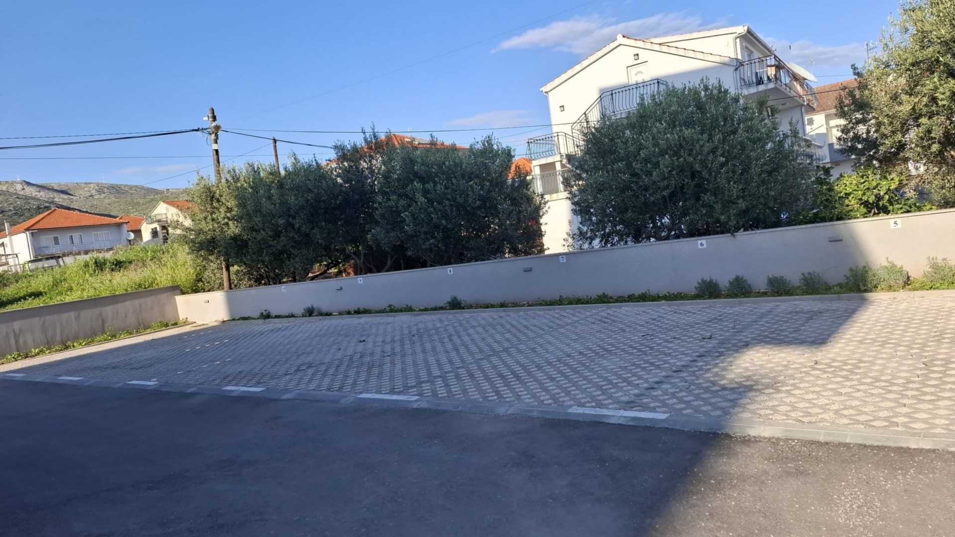Een verhard parkeerterrein met een lage muur en een gebouw met balkon op de achtergrond.