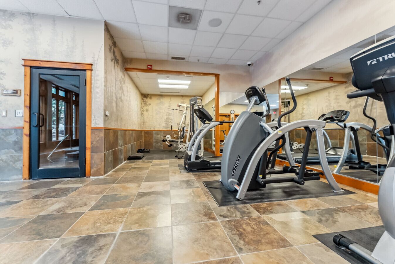 Une salle de sport équipée de matériel d’exercice, avec une porte et un sol carrelé.