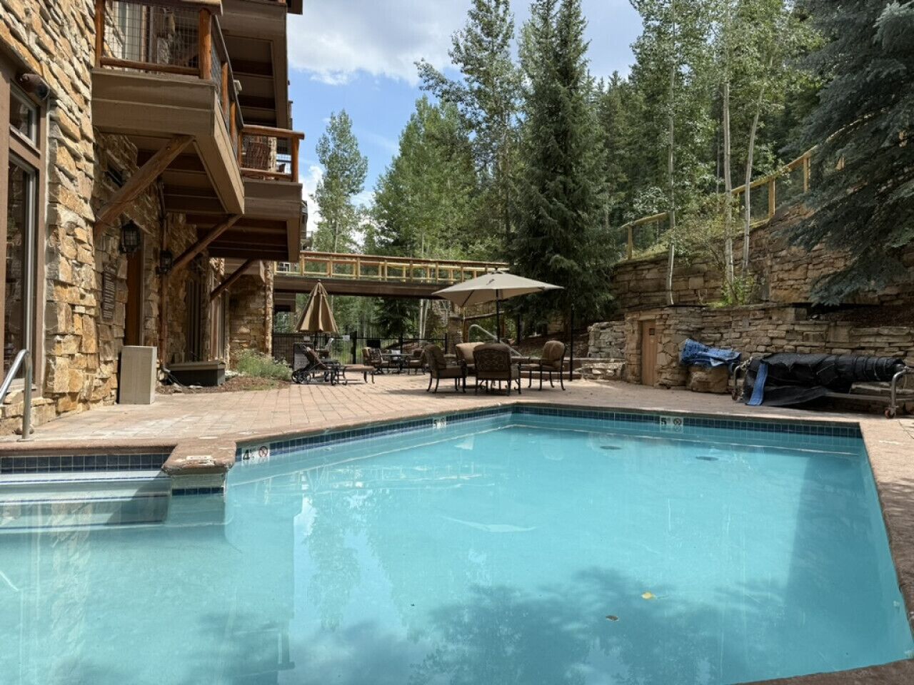 A swimming pool with a wooden deck, outdoor furniture, and a stone building with balconies.