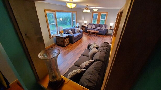 A cozy living room with a sofa, a coffee table, and a lamp. There are large windows and a door leading to another room. - Hale Eddy (Hancock)