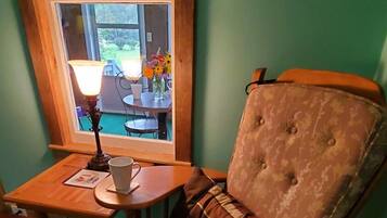 A cozy room with a wooden chair, a small table, and a window overlooking a garden.