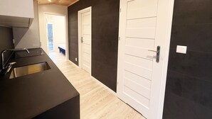 Une cuisine au design moderne, un couloir menant à une chambre, et un mur sombre avec une porte blanche.