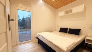 Une chambre à coucher comprenant un lit, une table de chevet, une étagère fixée au mur et une porte-fenêtre coulissante donnant sur un espace extérieur.