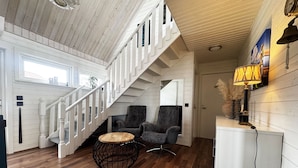 A spacious room with a wooden staircase, two armchairs, a round coffee table, and a white cabinet.