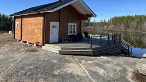 A wooden cabin with a porch and a dock extending into a lake, surrounded by trees. - Newly built log cabin with sauna located on a lakeside plot outside Hultsfred | SE05086 (Vena)