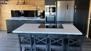 A modern kitchen with a central island, black cabinets, stainless steel appliances, and a wooden ceiling. - Newly built log cabin with sauna located on a lakeside plot outside Hultsfred | SE05086 (Vena)