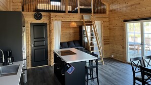 A cabin interior with a kitchen area, dining space, and a loft bedroom. - Newly built log cabin with sauna located on a lakeside plot outside Hultsfred | SE05086 (Vena)