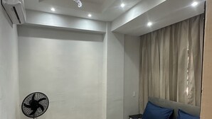A hotel room with a bed, a standing fan, and a ceiling light fixture.