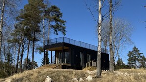 A modern cabin with a balcony, surrounded by trees and a grassy hill. - Holiday home in the middle of nature in Knäred |SE02014 (Knäred)