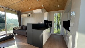 A modern kitchen with a central island, a built-in oven, and a large window overlooking a natural landscape. - Holiday home in the middle of nature in Knäred |SE02014 (Knäred)