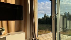 A modern room with a TV mounted on a wooden wall, a sliding glass door leading to an outdoor deck, and a minimalist white console table. - Holiday home in the middle of nature in Knäred |SE02014 (Knäred)