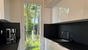 A modern kitchen with a built-in coffee maker, a sink, and a view of a forest through a glass door. - Holiday home in the middle of nature in Knäred |SE02014 (Knäred)